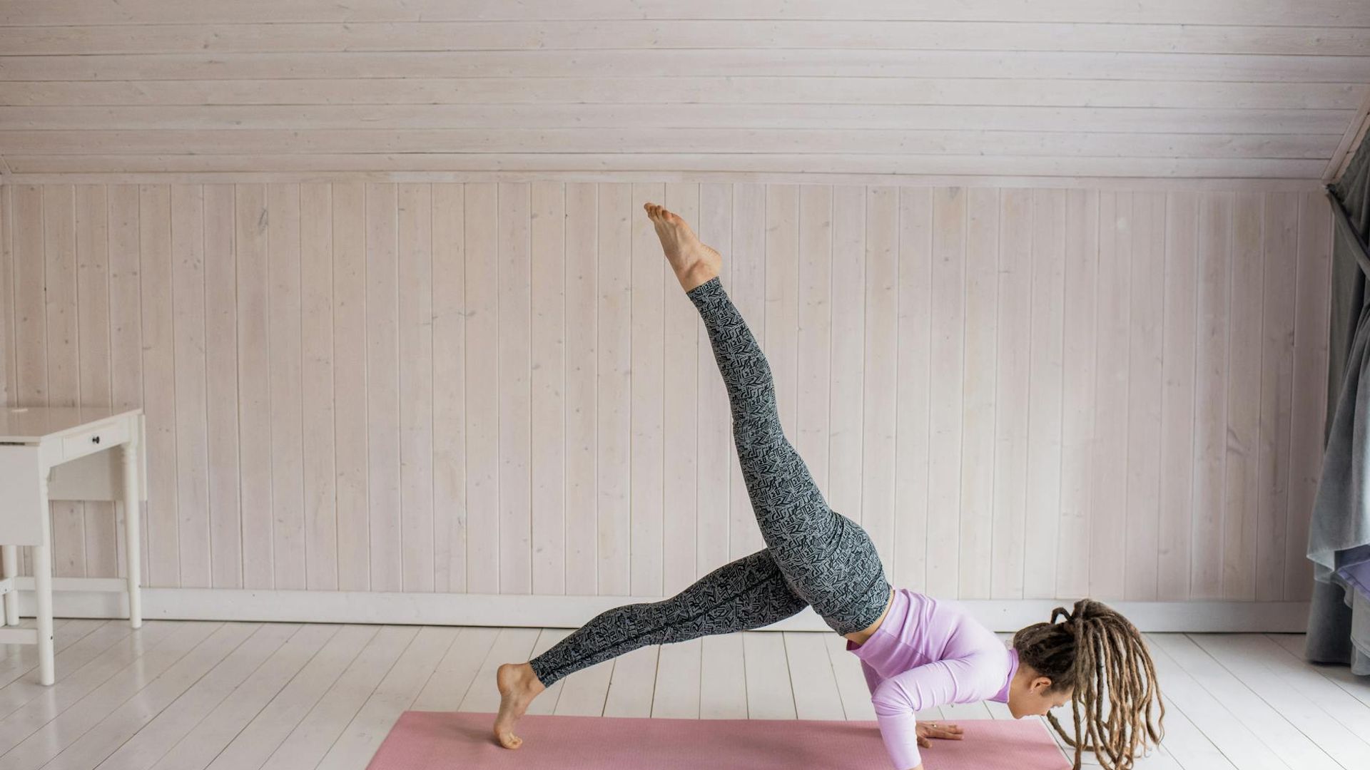 Person practicing yoga in a dark room with pink neon light.